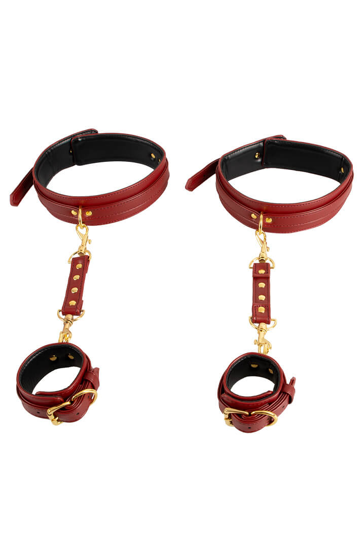 Red faux leather restraint cuffs linking wrists to thighs with snap hooks