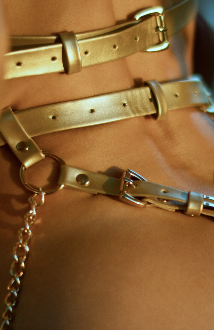 Metallic gold body harness with adjustable straps and chains at the hips